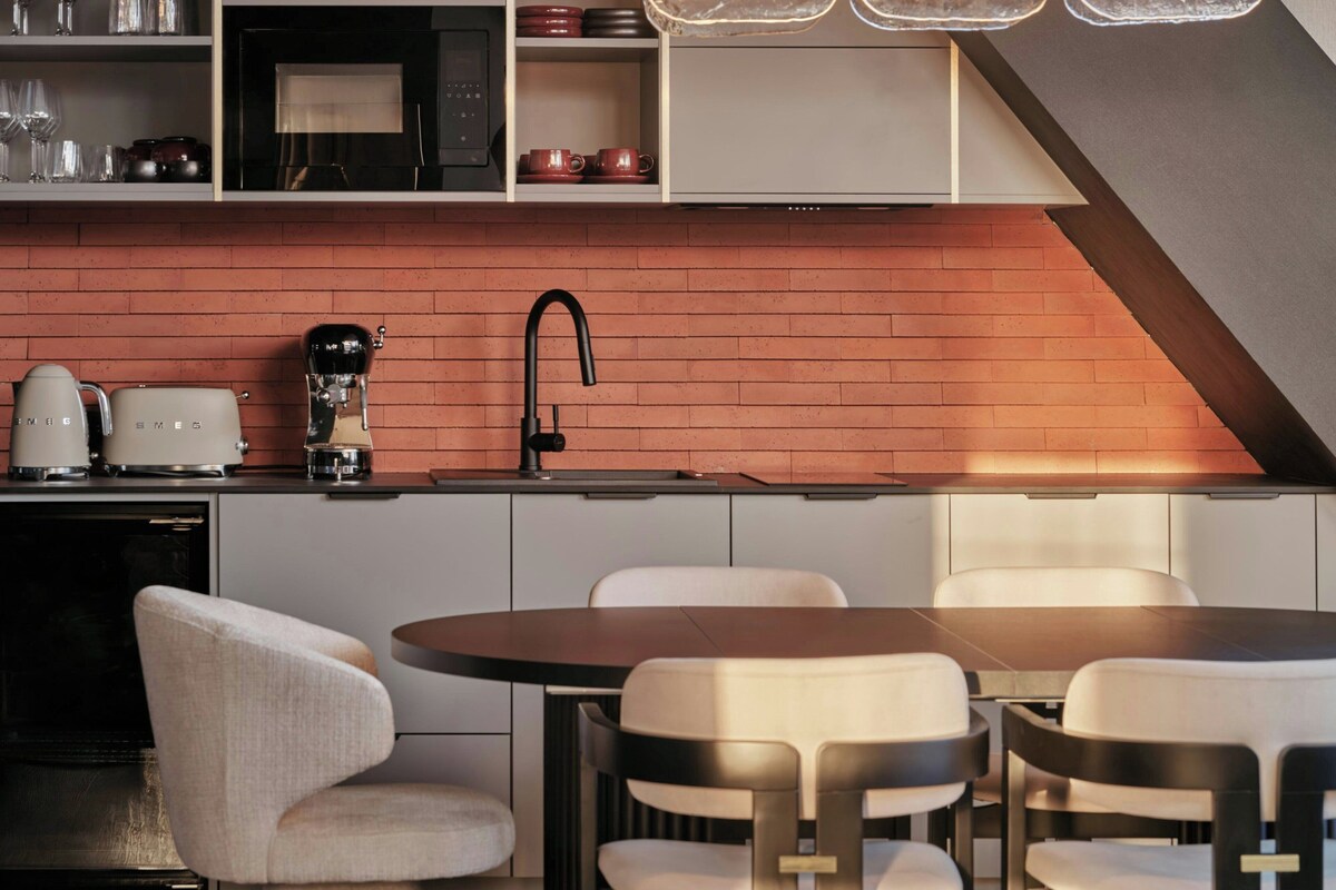 A modern kitchen with a brick backsplash, a sink, and a dining area with chairs.