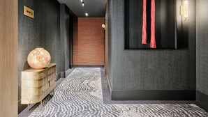 A modern interior with a dark wall, a wooden cabinet, a patterned rug, and a wall-mounted light fixture. - The Brick, a Tribute Portfolio Hotel - Adults Only (Gdansk)