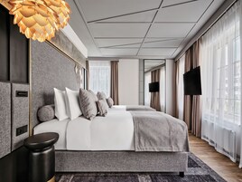 Una habitación de hotel moderna con una cama grande, un televisor de pantalla plana y un amplio ventanal con cortinas.