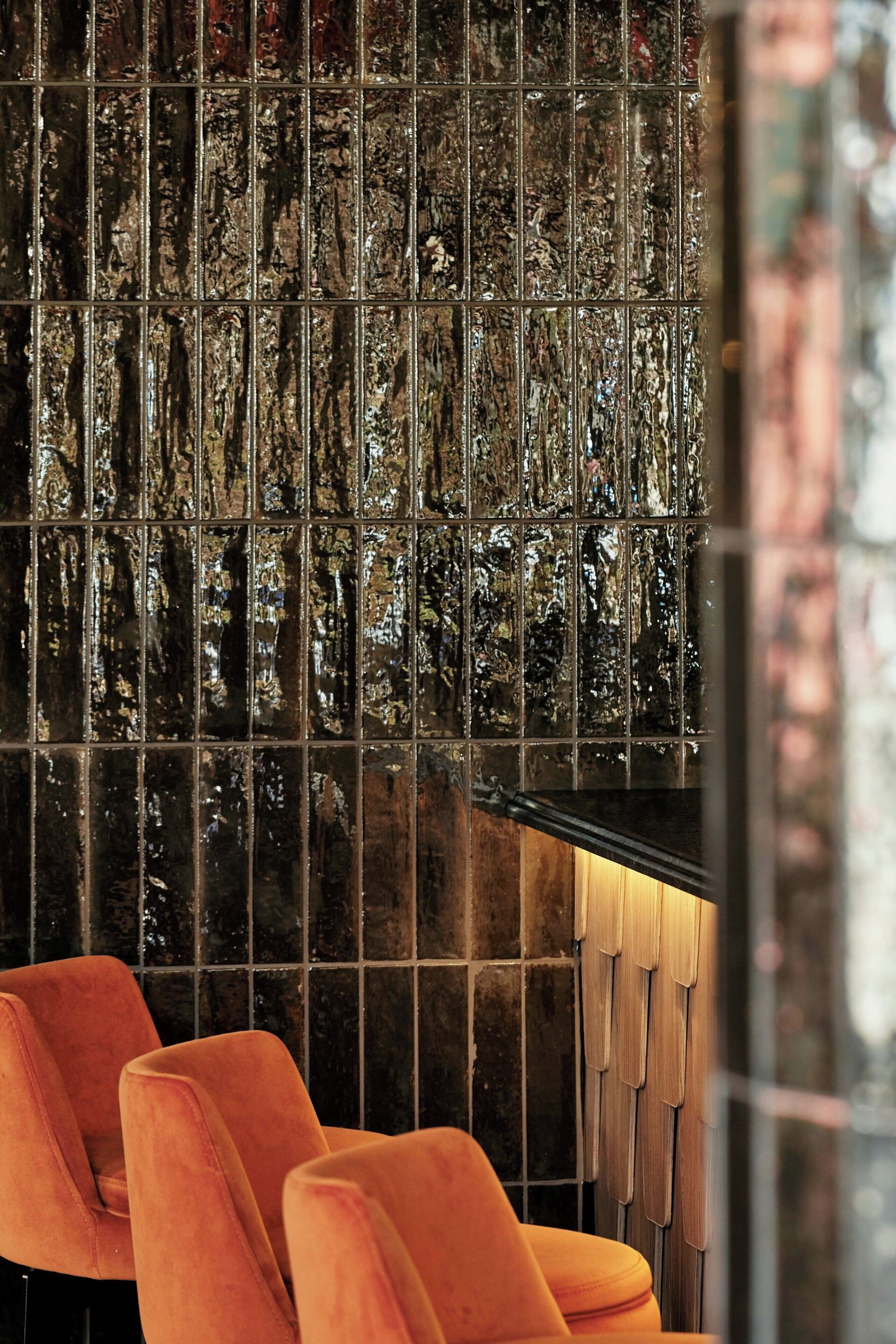 A bar area with a textured wall and orange chairs.