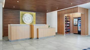 A reception area with a wooden reception desk, a wall-mounted decorative piece, and a vending machine stocked with snacks.