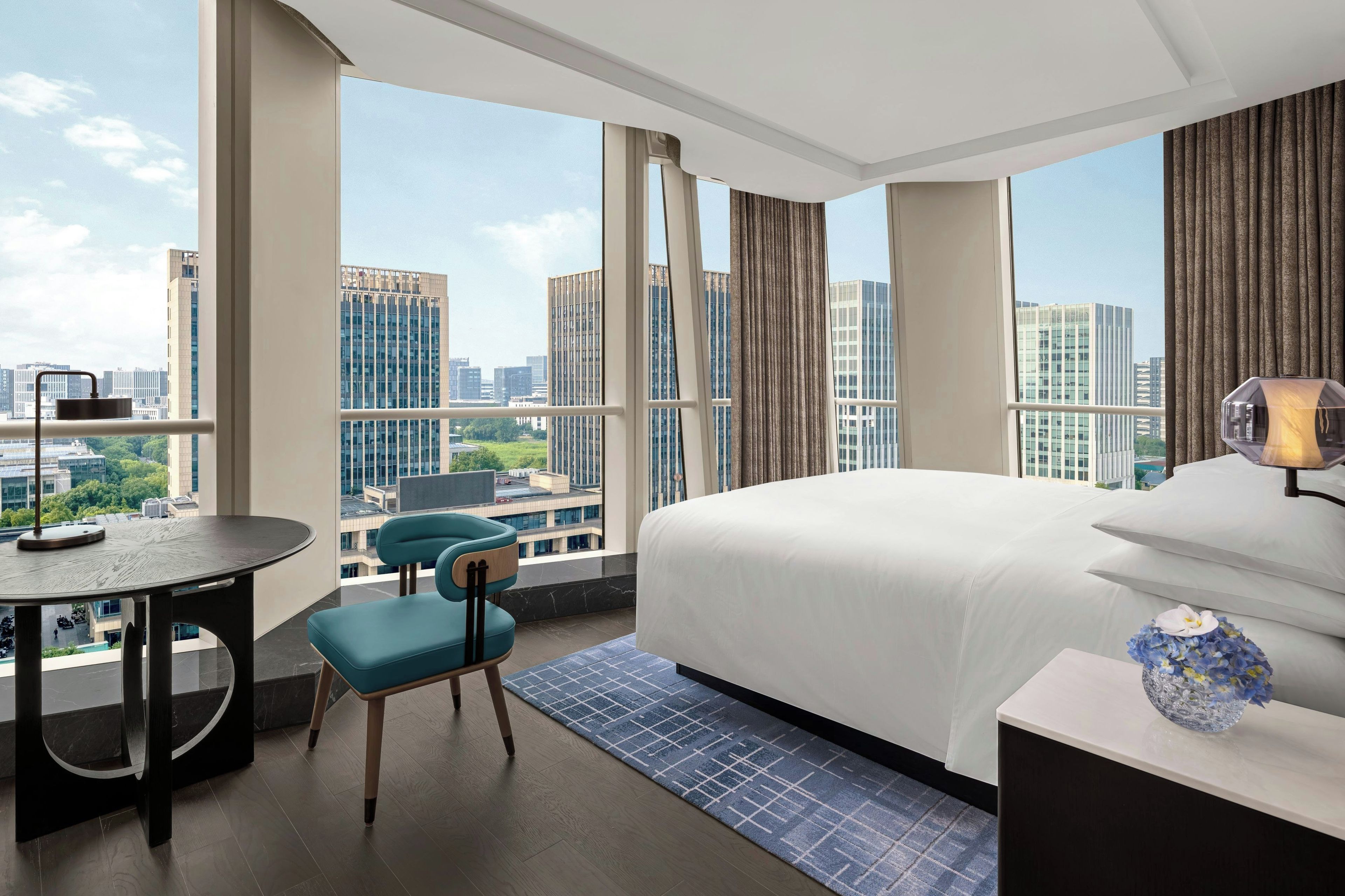 A hotel room with a large bed, a desk, a chair, and a view of the cityscape.