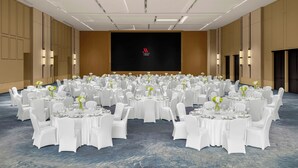 A large conference room with round tables, white chairs, and a black screen with a logo in the center. - Marriott Shanghai Hotel Songjiang (Shanghai)