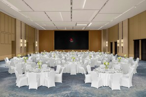 A large conference room with round tables, white chairs, and a black screen with a logo in the center. - Marriott Shanghai Hotel Songjiang (Shanghai)