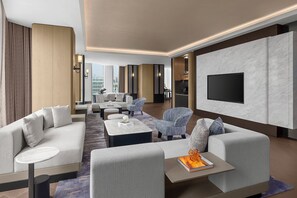 Quarto de hotel moderno com área de estar, televisão de tela plana na parede e vista para a cidade.