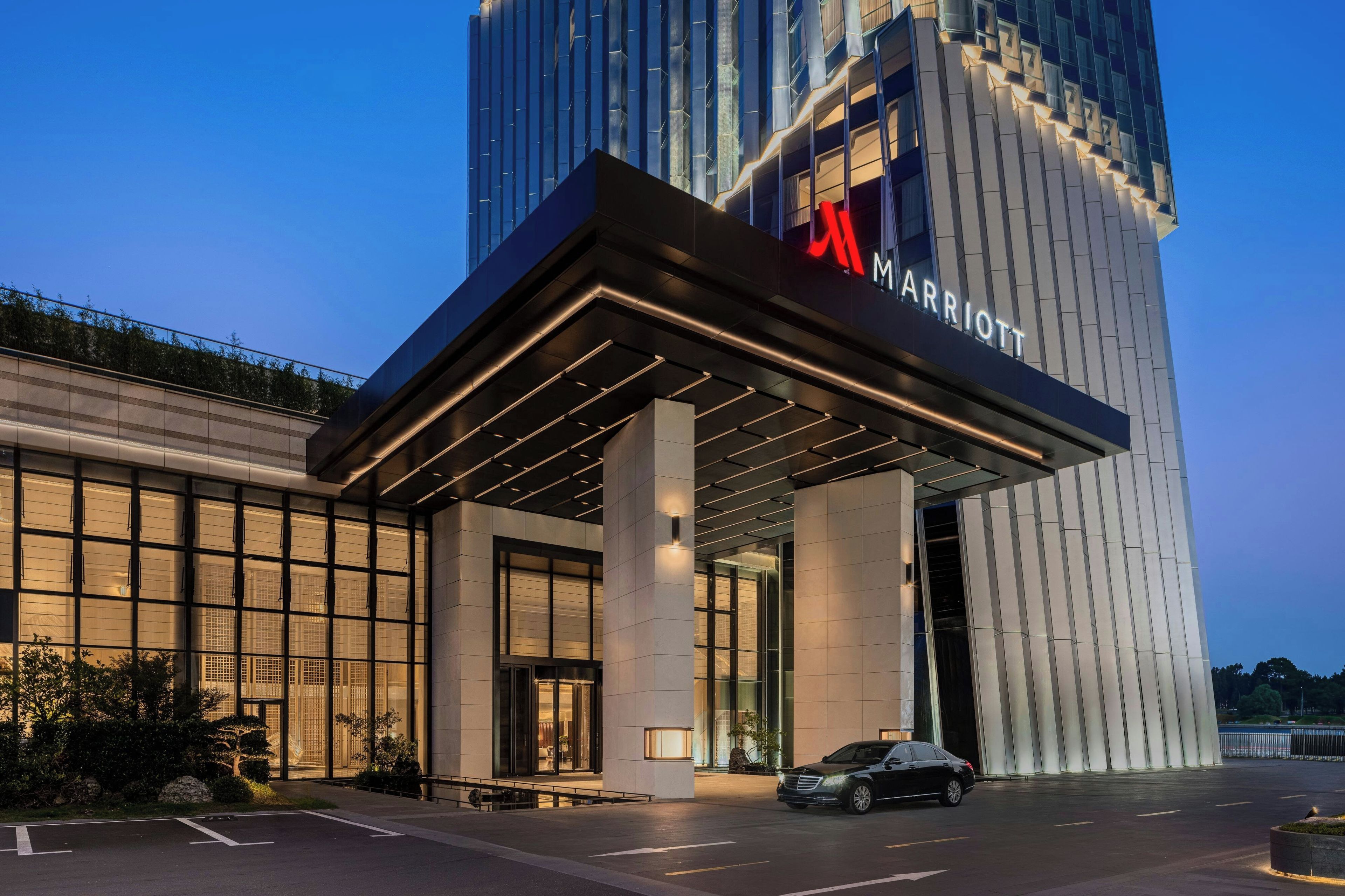 A modern hotel entrance with a prominent sign, a covered driveway, and a car parked in front.