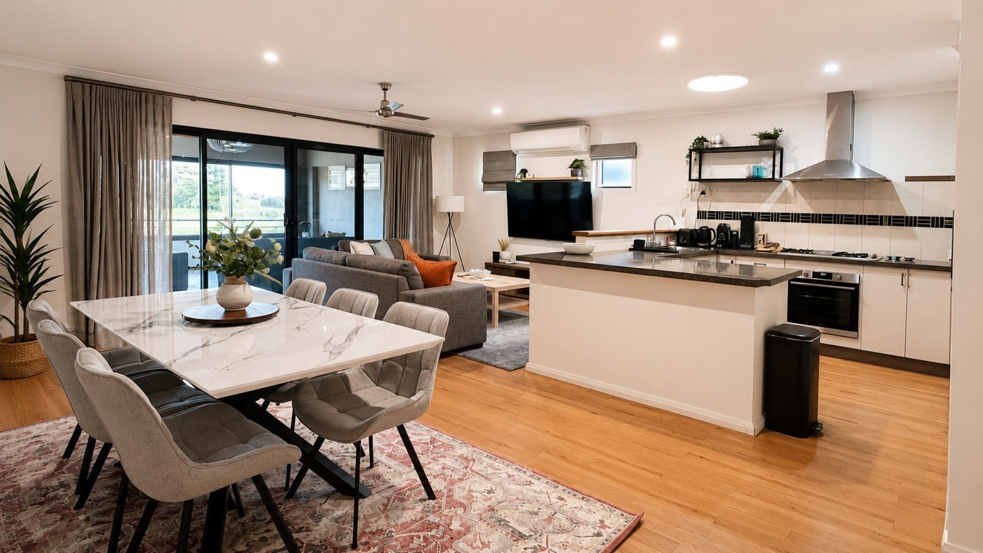 A modern apartment with a dining area, sofa, kitchen, and a large TV.