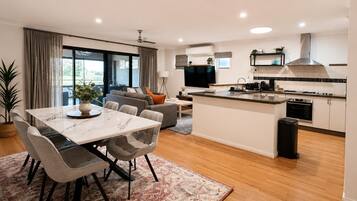 A modern apartment with a dining area, sofa, kitchen, and a large TV.