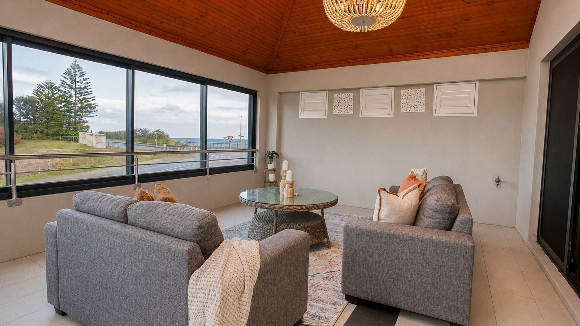 A modern living room with a large window, grey sofas, a round coffee table, and a wooden ceiling.