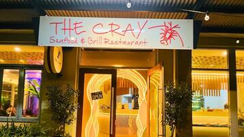 The exterior of The Cray Seafood & Grill Restaurant with a neon sign and a glass door entrance.