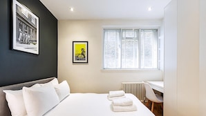 Un dormitorio con cama, escritorio, silla, radiador y dos cuadros en la pared.