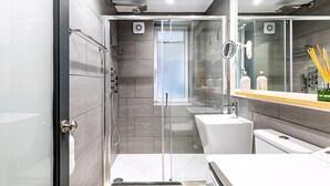 Un baño moderno con ducha de vidrio, un lavabo blanco y un espejo grande.