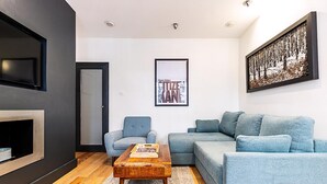 Una sala de estar moderna con un sofá gris, un sillón azul, una mesa de centro de madera y un cuadro enmarcado en la pared.