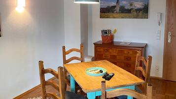Ein Essbereich mit Holztisch, Stühlen, einer Pendelleuchte, einem Gemälde an der Wand und einem Holzschrank.
