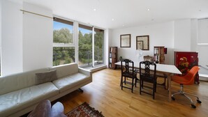 A modern living room with a sofa, dining table, chairs, and large windows. - Regent's Canal View Apartment (London)