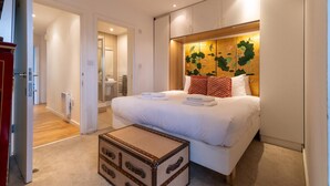 A bedroom with a bed, a suitcase, and a wall with a floral design. - Regent's Canal View Apartment (London)