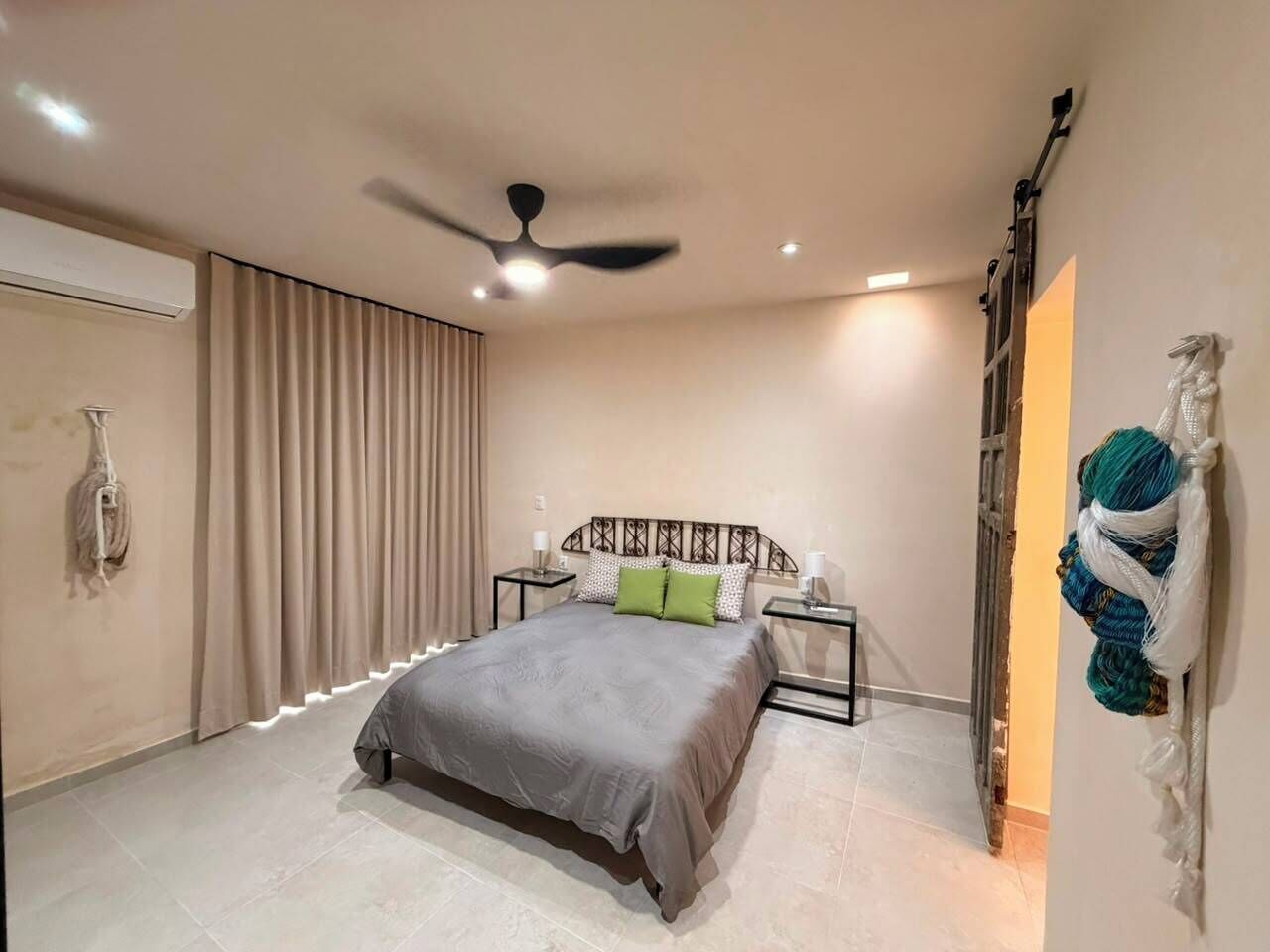 Ein Schlafzimmer mit einem Bett, einem Deckenventilator, einem Nachttisch und einer Wandleuchte.