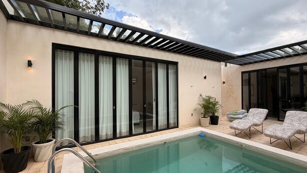 Ein moderner Poolbereich mit klarem Pool, einer überdachten Terrasse und einer Glastür zum Schlafzimmer.