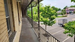 A covered outdoor area with a metal railing, a brick building, and a view of a parking lot and greenery.