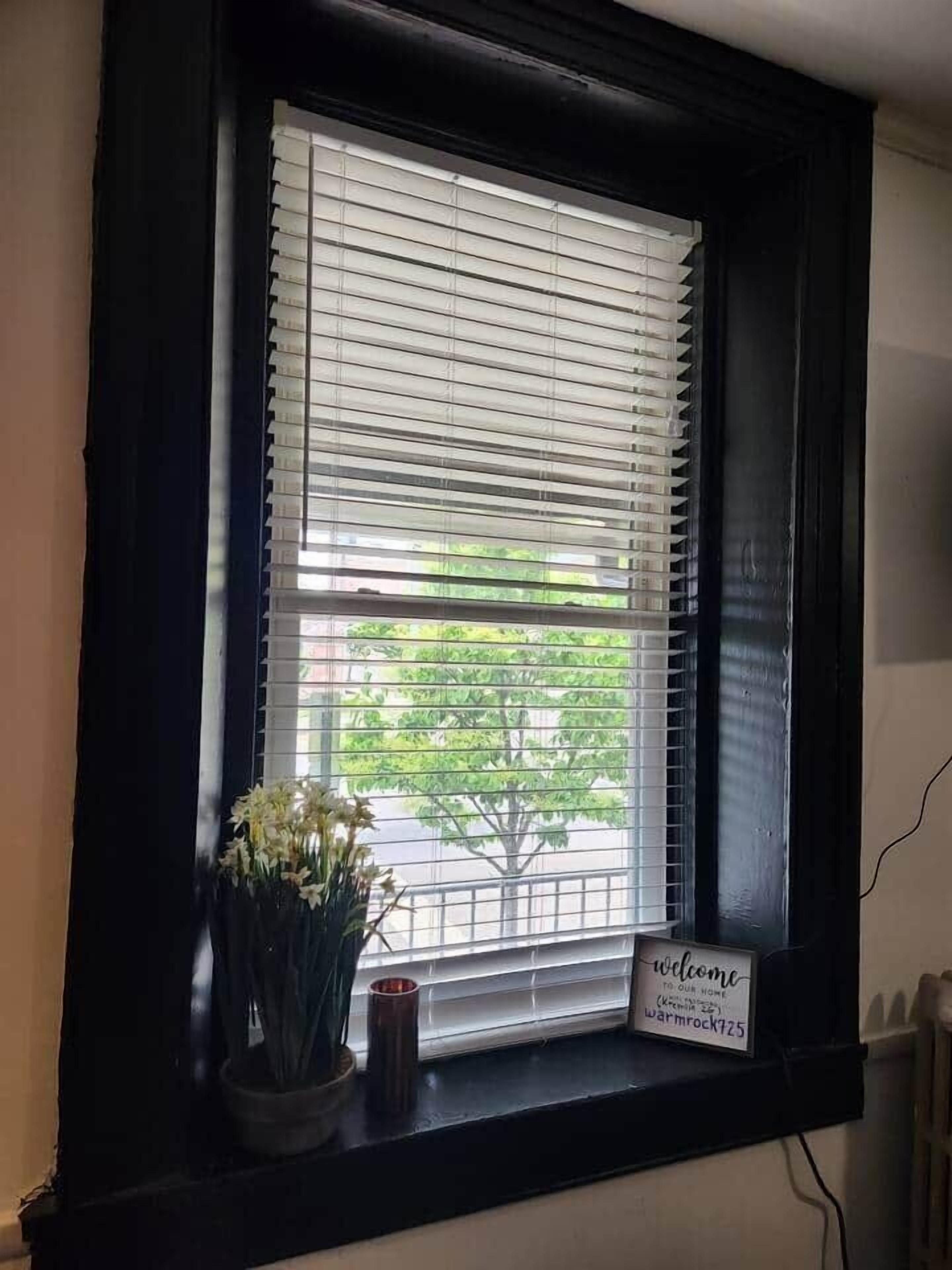 Una ventana con persianas, un cartel de bienvenida y una planta en maceta.