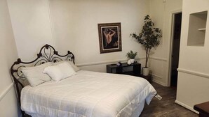 A bedroom with a bed, a nightstand, a potted plant, and a framed picture on the wall.