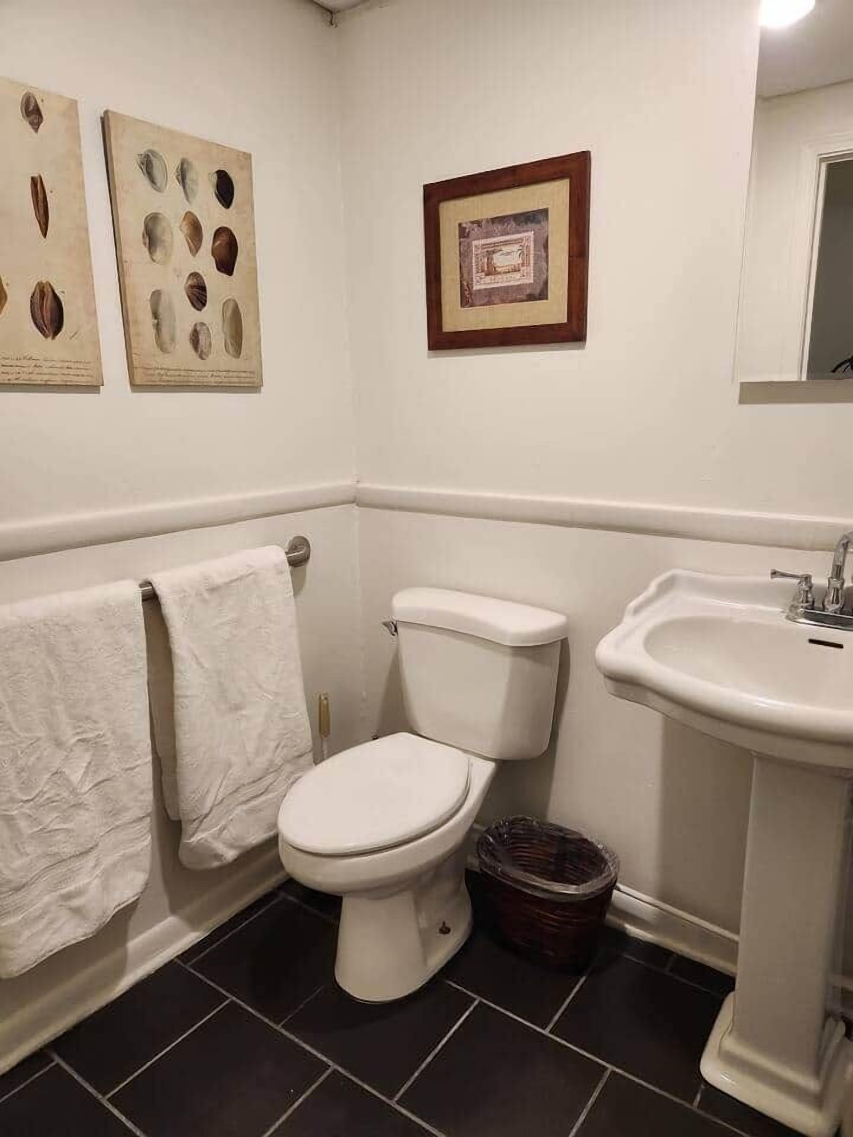Un baño con inodoro, lavamanos y dos cuadros en la pared.