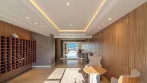 A modern hotel lobby with a wooden wall, a seating area with a round table, and a shelving unit with bottles. - Apt in Downtown Blumenau Building Une1105 (Blumenau)