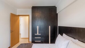 A bedroom with a bed, a dark wardrobe, and a wooden door. - Apt in Downtown Blumenau Building Une1105 (Blumenau)