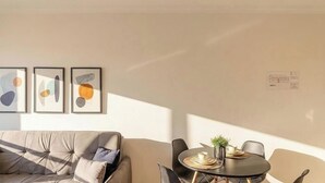 A modern living room with a sofa, a dining table with chairs, and abstract wall art. - Apt in Downtown Blumenau Building Une1105 (Blumenau)
