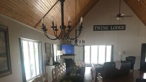 Ein langer Esstisch mit Stühlen, eine Chandelüster, ein Fernseher und ein Schild mit der Aufschrift 'TWINS LODGE'.