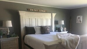 Ein Schlafzimmer mit einem großen Bett, zwei Nachttischen, einer Kommode und einem Schild über dem Bett mit der Aufschrift 'TWINS LODGE'.