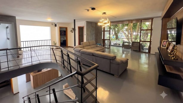 Amplia sala de estar con un sofá moderno, una escalera y un balcón.