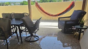 A covered patio with a table and chairs, a hammock, and a view of the cityscape. - Paradise Penthouse at Aquatika Loiza (Vieques)