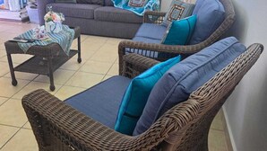 A living room with wicker furniture, a grey sofa, and a blue and white patterned throw. - Paradise Penthouse at Aquatika Loiza (Vieques)