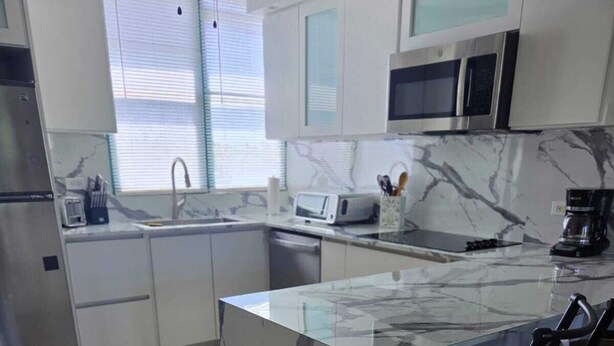 A modern kitchen with a marble island, bar stools, a microwave, and a coffee maker. - Paradise Penthouse at Aquatika Loiza (Vieques)