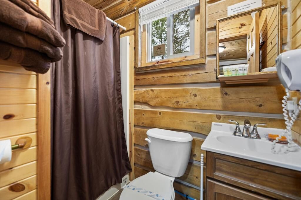 Baño de cabaña de madera con inodoro, lavamanos y ventana.