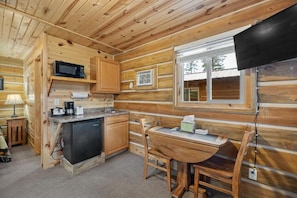 A log cabin interior with a kitchen area, a dining table, and a television. - Black Hills Trailside Park Resort (Hill City)
