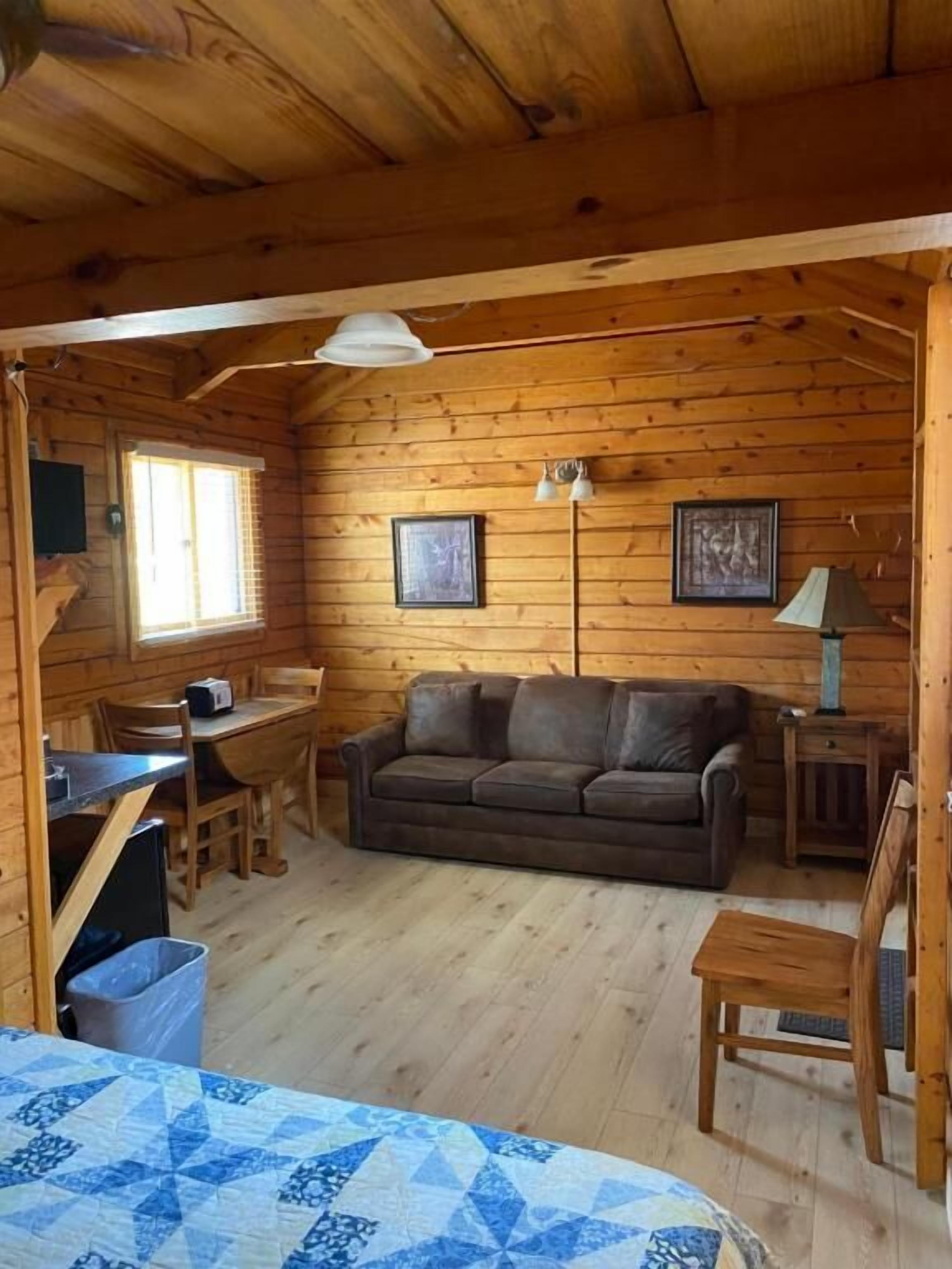 A wooden cabin interior with a sofa, a dining table, and a lamp.