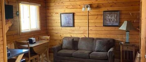 A wooden cabin interior with a sofa, a dining table, and a lamp.