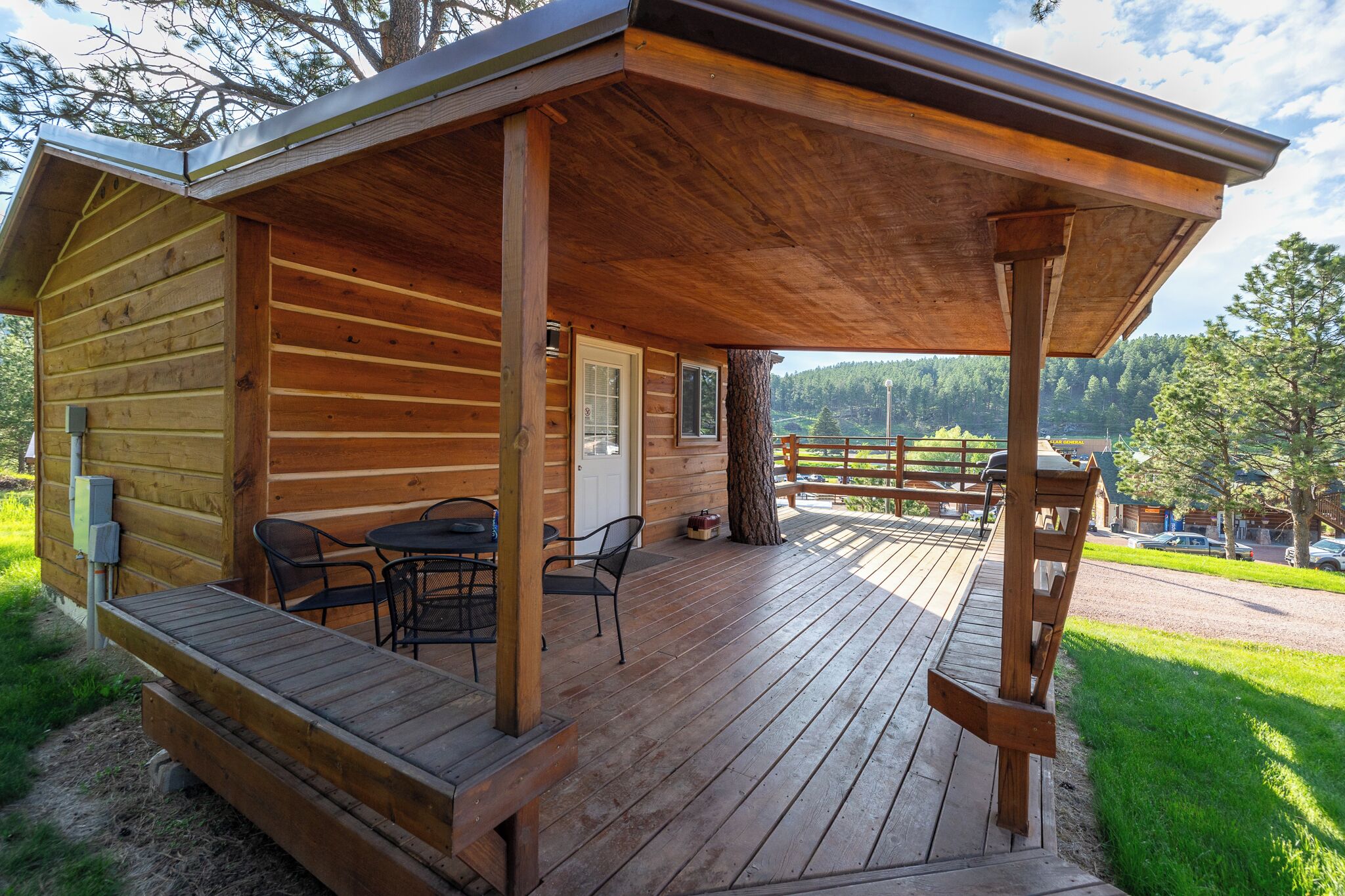 A wooden cabin with a covered deck, outdoor seating, and a view of the surrounding landscape.