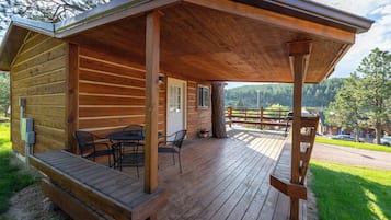 A wooden cabin with a covered deck, outdoor seating, and a view of the surrounding landscape.