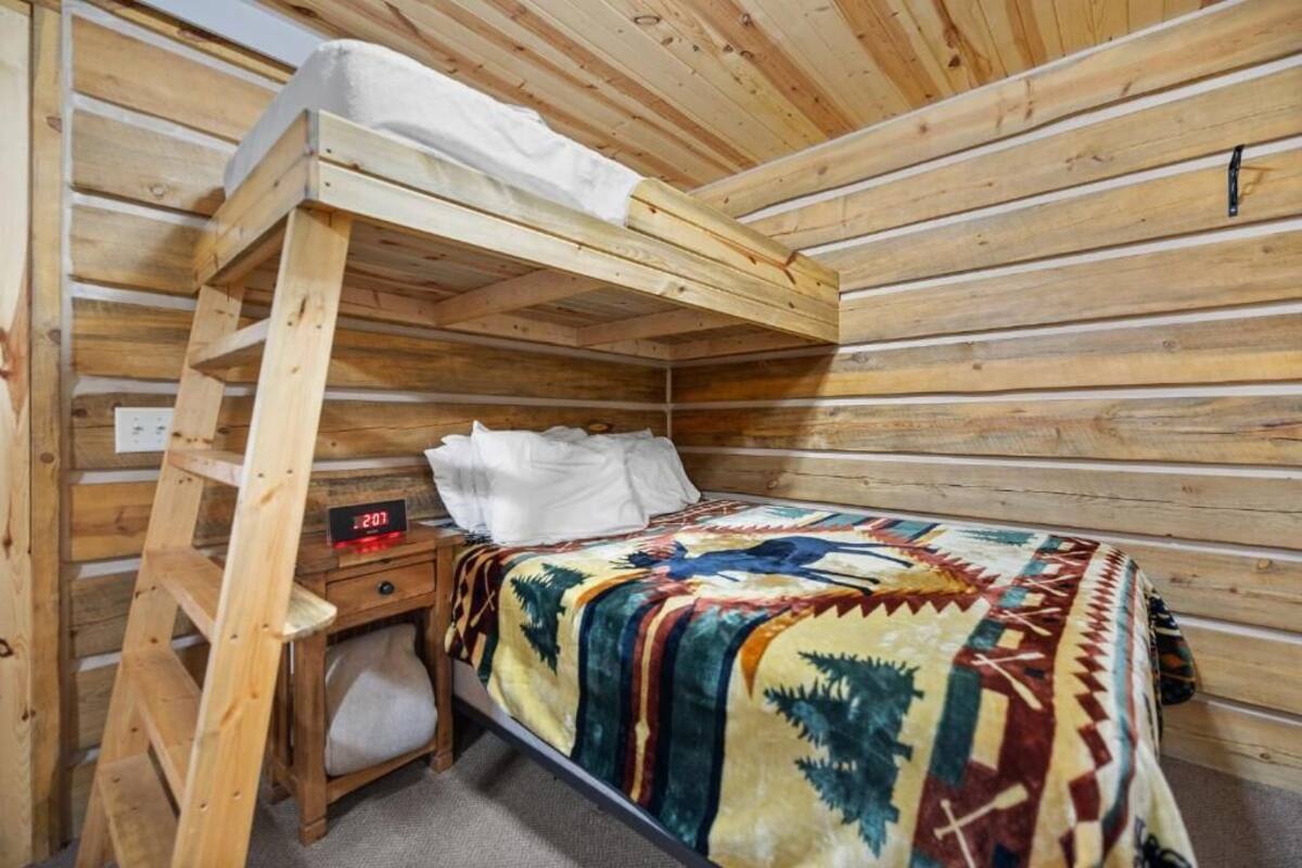 Una habitación de cabaña de madera con una cama litera, una mesita de noche con un reloj y una manta estampada.