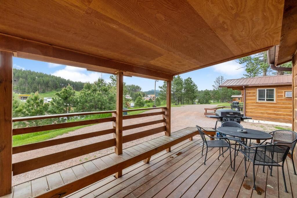 A wooden deck with a bench and outdoor seating, overlooking a forested area.