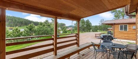 A wooden deck with a bench and outdoor seating, overlooking a forested area.