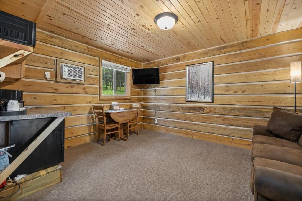 A cabin interior with a wooden interior, a television mounted on the wall, a small table with chairs, and a sofa.