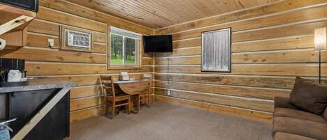 A cabin interior with a wooden interior, a television mounted on the wall, a small table with chairs, and a sofa.