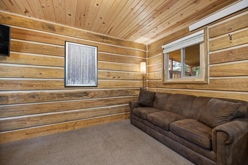 L’intérieur d’une cabane en rondins, avec un canapé marron, un tableau encadré et une fenêtre donnant sur un paysage.
