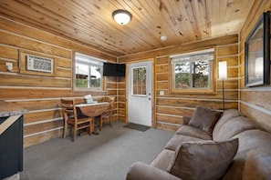 A log cabin interior with a dining area, a sofa, and a television mounted on the wall. - Black Hills Trailside Park Resort (Hill City)