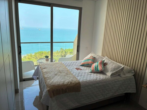 Ein Schlafzimmer mit Bett, Kissen, Nachttisch und Meerblick.