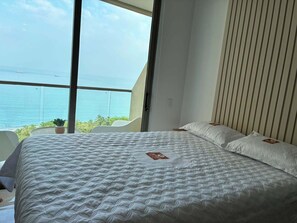 Ein Schlafzimmer mit einem großen Bett, Blick auf den Ozean und einer Zimmerpflanze.